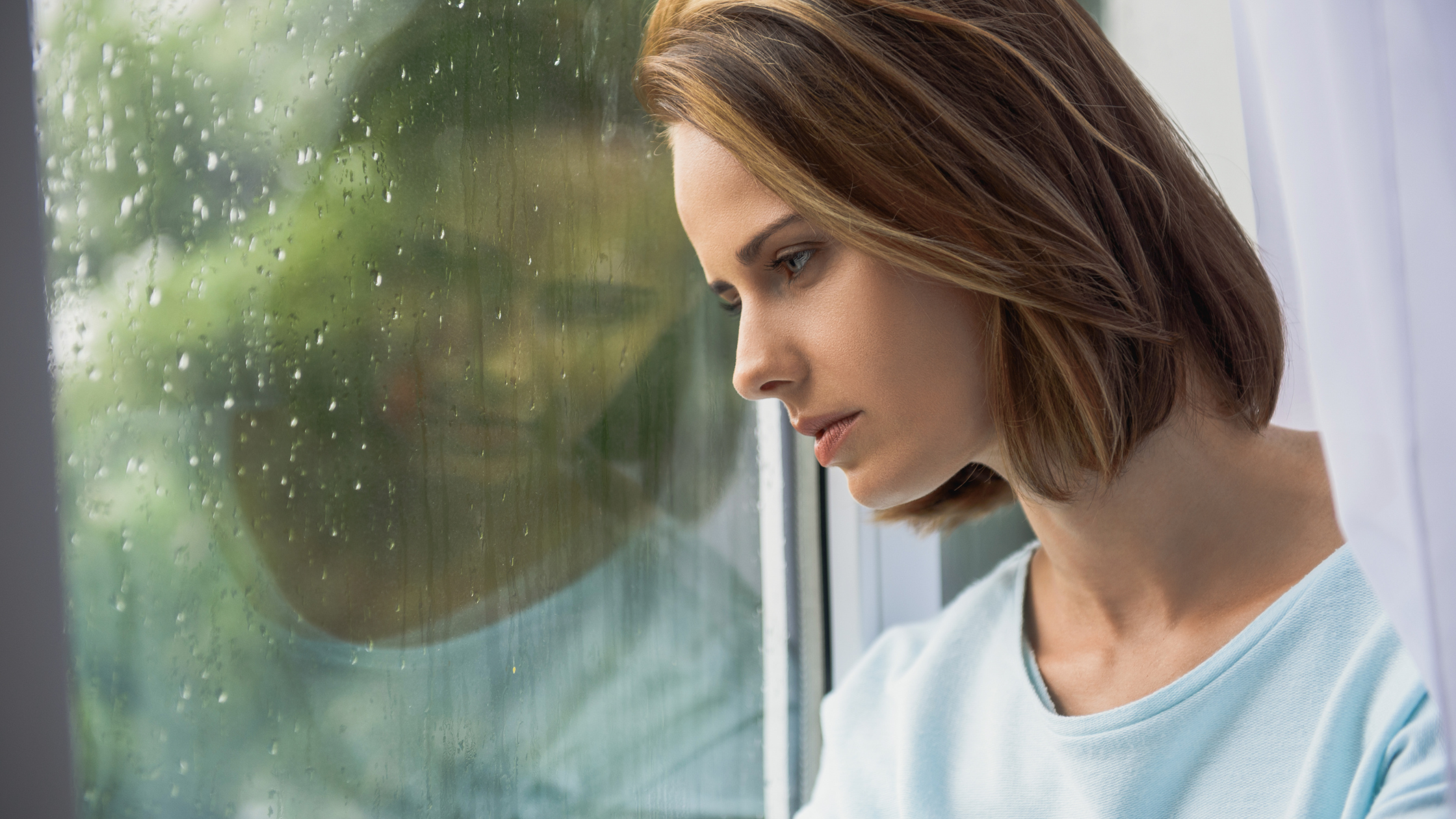 Sad woman gazing out of rainy window