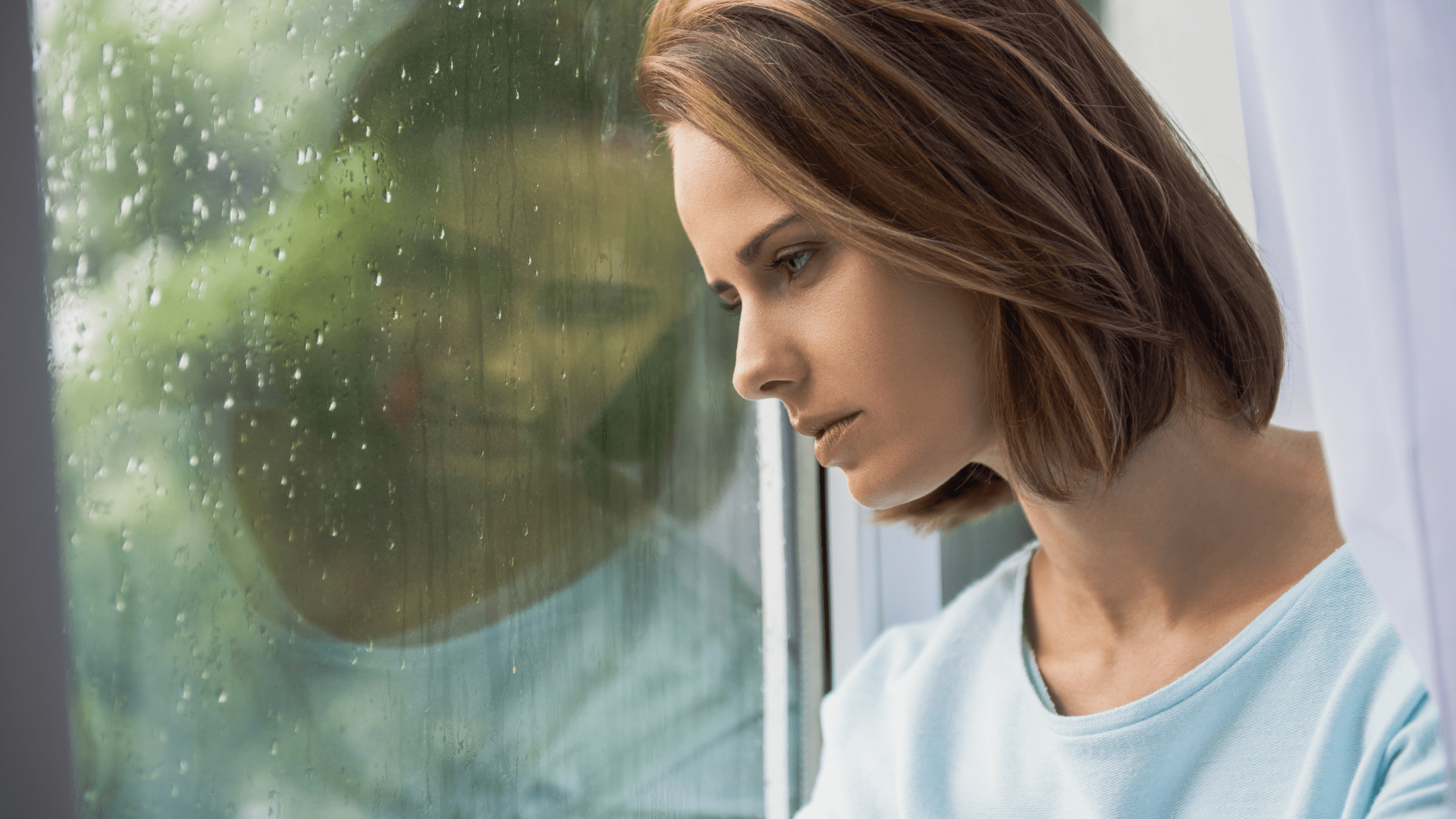 Sad woman gazing out of rainy window