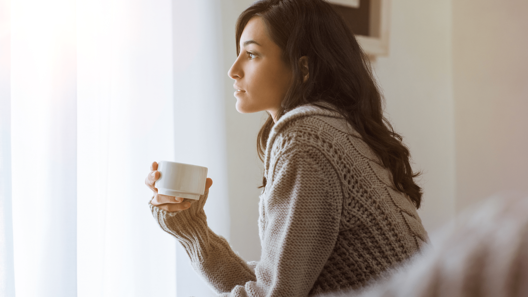 Young girl thinking with a cup of coffee looking out the window