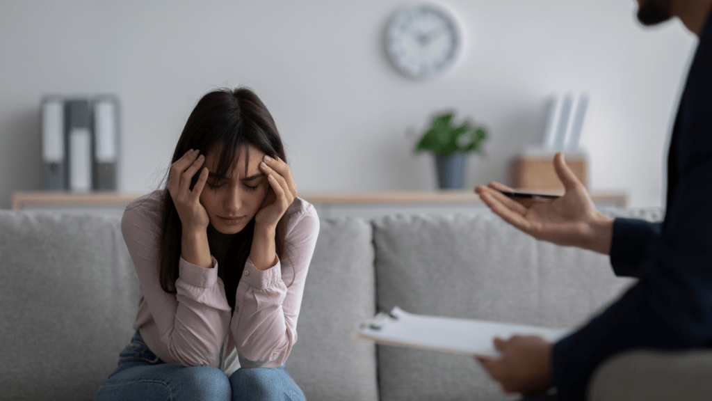 Female counselor writing on notepad while depressed woman sitting with head in hand at office during therapy session